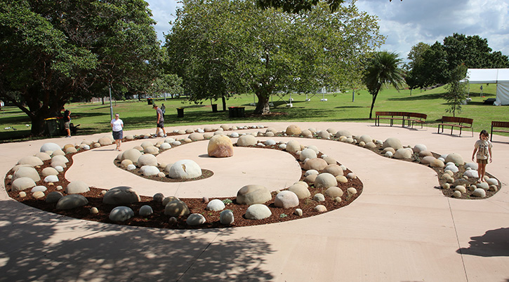 People wandering though an artwork in a park made up of large sandstone boulders arranged in a spiral
