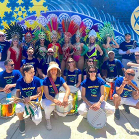 A group of drummers in blue shirts in front of a mural