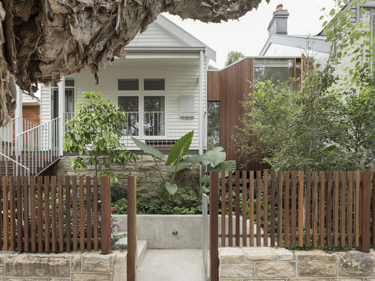 The front of a renovated single-family home. There are two distinct parts of the building: an original part in white cladding, and a modern extension in dark timber.