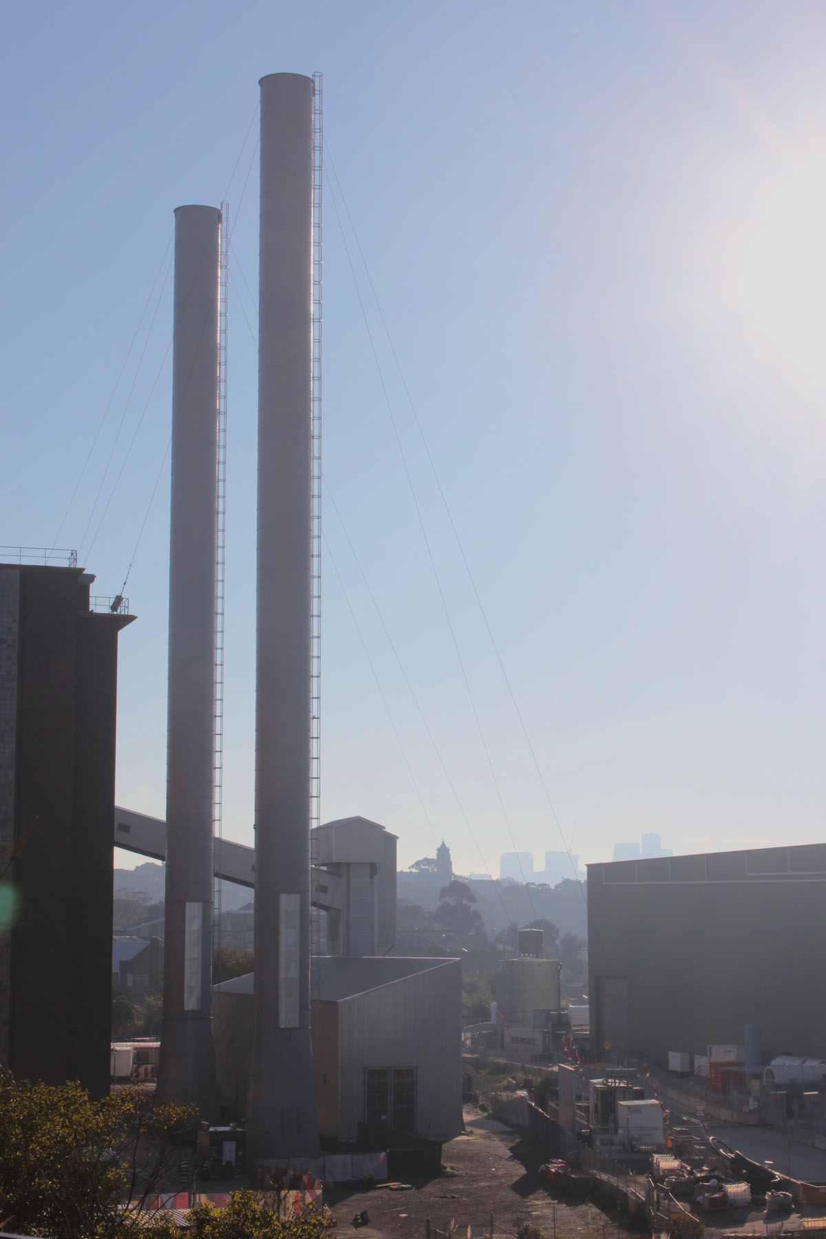 Two tall cylindrical industrial towers, situated closely together, rise dramatically into the blue sky.