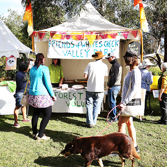 people gathered around a trestle table with a hand painted sign
                        that reads 