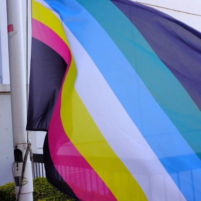 Cloe up of disability pride flag unfurling in the wind showing red, gold white, blue and green stripes.