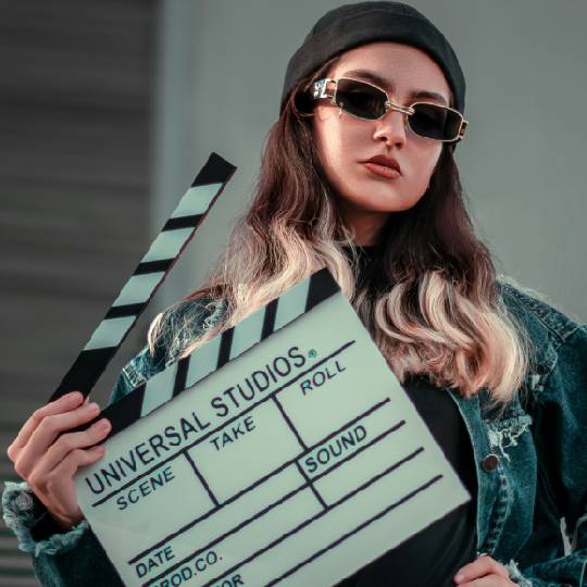 Young person wearing sunglasses holding a film clapper board