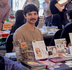 young person sitting at a table surrounded by comics