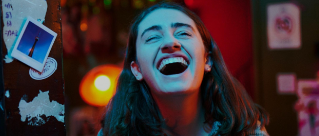 Close up of person laughing with eyes closed, their face is bathed in blue light