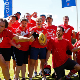 A group of cheerful men and women in red AFL jerseys on a sports field 