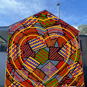 A vibrant coloured Aborigal  mural consisting of lines, dots and large hearts on the side of a house