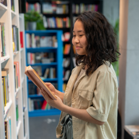 Young woman reading a book by  a bookshelf