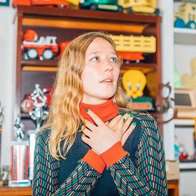 Singer Julia Jacklin in 60s style sweater turtleneck orange and blue design, long orange wavy hair, hands crossed on chest photo