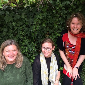 Three performers sitting in front of green wall vine