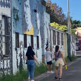 Photo of three people walking down a lane, there are murals on the wall to left hand side