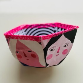 Close up of a small handmade paper bowl with cartoon faces and bright pink decorate tape. 