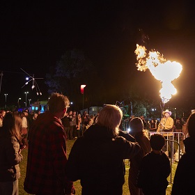 Photo of EDGE Sydenham by Shane Rozario, presentation by Tortuga Studios a nighttime photo an artist holding a fire hose with fire emitting out of it, a large crowd stands around watching