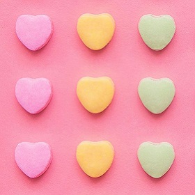 Cropped photo or illustration of baby pink background with pastel row of three heart stacked ontop of each other, 3 row of hearts colour include pink, orange and green, 