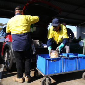 two men taking paint out of car for recycling