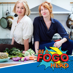 Two women sitting on kitchen bench with fresh fruit and veggies