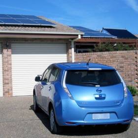 Small blue car in driveway of house with solar panels on roof