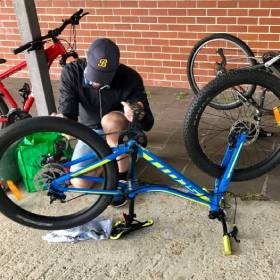 Man in blue cap cleaning his bike which is upsidedown