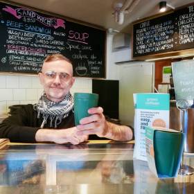 Man holding green reusable coffee cup in cafe