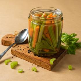 Glass jar filled with sticks of celery and carrot on a chopping board with a spoon