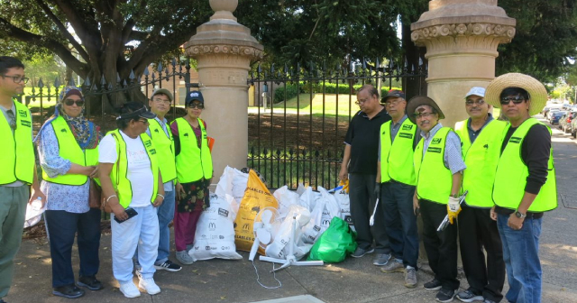 Group of people in flouro yellow jackets standing around a pile of bags with Clean Up Australia Day symbols on them