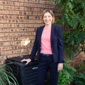 Woman in suit stands next to a backyard compost bin