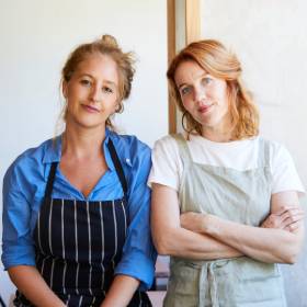 Two women in chefs aprons standing side by side