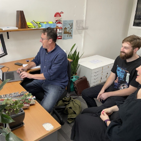 people sitting around a desk chatting and looking at a computer