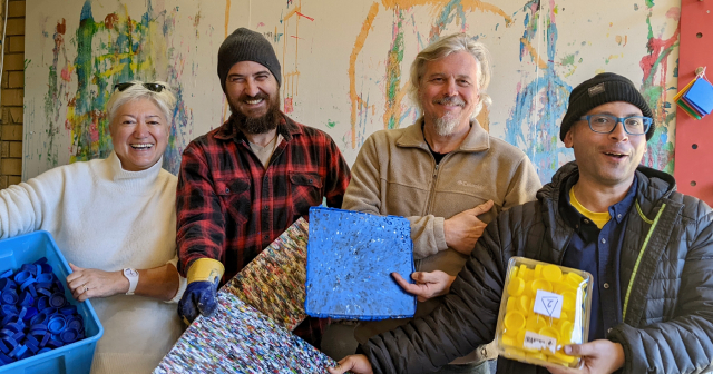 Four people standing together laughing and holding up plastic items