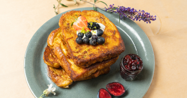 Three slices of toast with berries and jam on a round teal coloured plate