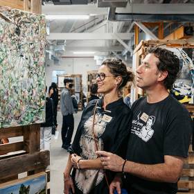 A woman and a man standing and looking at a piece of art, with people in the background