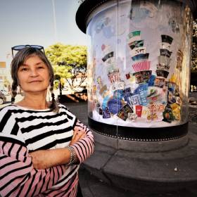 Woman with arms crossed stands in front of artwork of food packaging waste