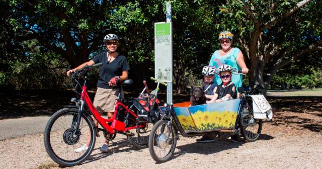 two women on bikes with two children and dog sitting in basket on front