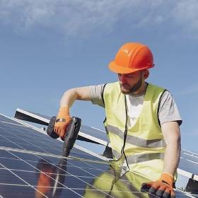 Man in orang hard hat and yellow vest using drill to set up solar panels