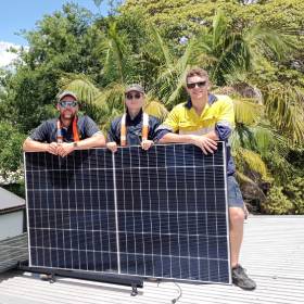 3 men standing on roof with solar panel