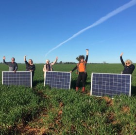 People in a field with solar panels behind them