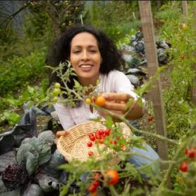 woman crouching in garden holding wooden basket and tomatoes