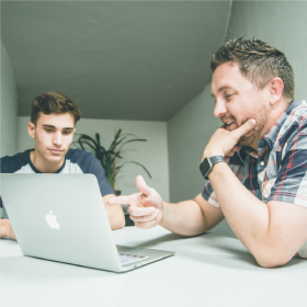 two men looking at a laptop and discussing something