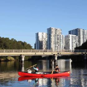 two people in kayak on river with buildings in background