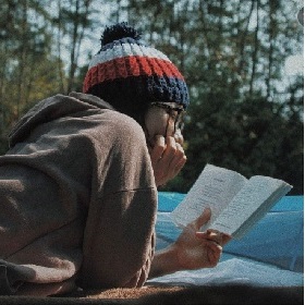 A woman in a beanie reading outside a tent