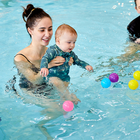 Parent holding up baby playing with colourful balls floating in the water