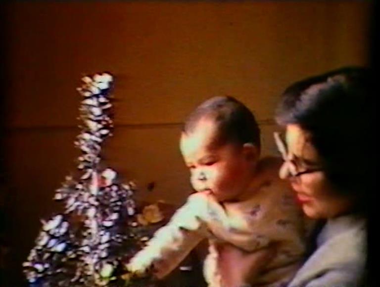 A parent holding an infant child who is reaching for a Christmas tree.