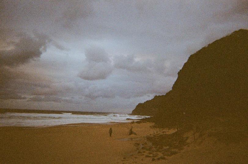 A dark film photograph of a cliffside beach under heavy cloud.