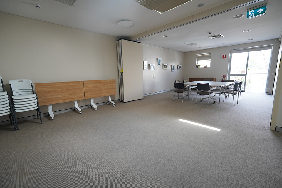 A long meeting room with a a table and stacked chairs against one wall, and eight chairs arranged around a meeting table in the background.