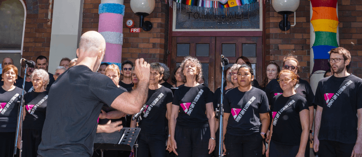 Sydney Gay and Lesbian Choir singing outside the Inner West Pride Centre decorated in LGBTQ pride and trans colours