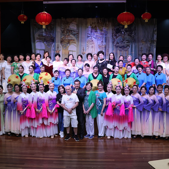 A large group of assembled performers posing for a photograph, with traditional Chinese lanterns in the background.