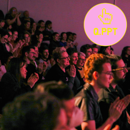 crowd bathed in pink light. A pink and yellow circular logo is in the corner of the image that reads Q.PPT with a computerised drawing of a hand