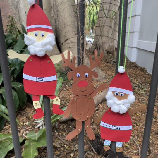 Mixed-media cutout decorations of Santa and Rudolph attached to a metal yard gate.