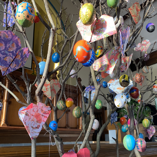 Many colourful painted eggs hung decoratively from an old tree branch
