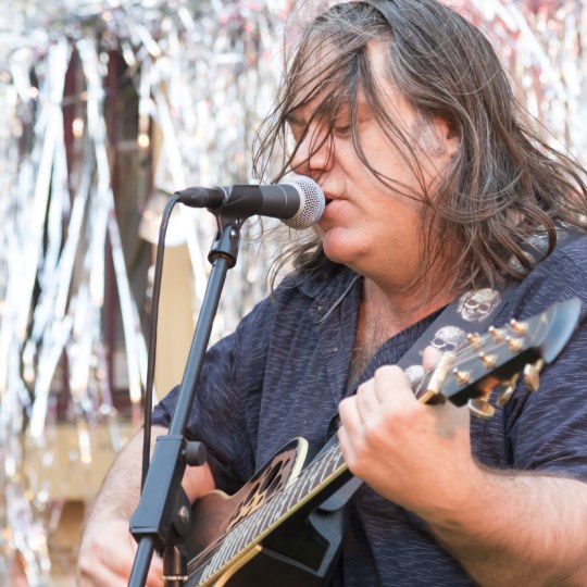 Shannon O'Connor playing guitar on stage, tinsel background, long hair blowing in wind